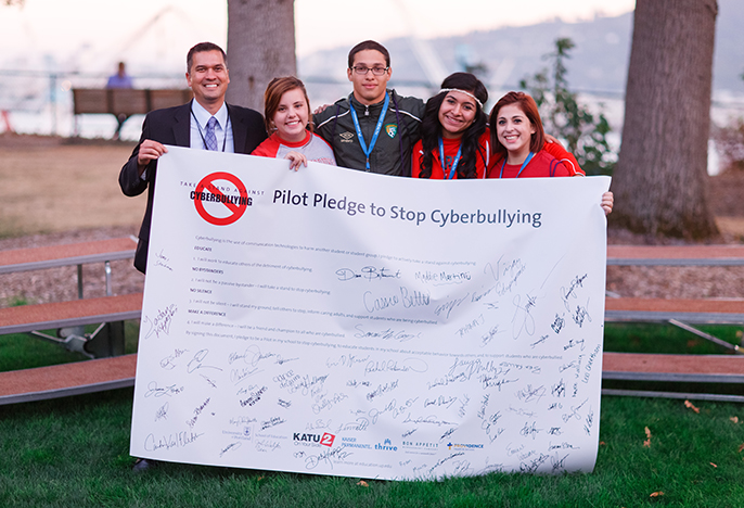 4 four students and a professors holding a banner: Pilot Pledge against Cyberbullying